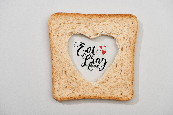 Κάτοψη του ψωμιού φέτα με σκαλιστή καρδιά και τρώνε, προσεύχονται, αγάπη γράμματα σε γκρι φόντο - Φωτογραφία, εικόνα
