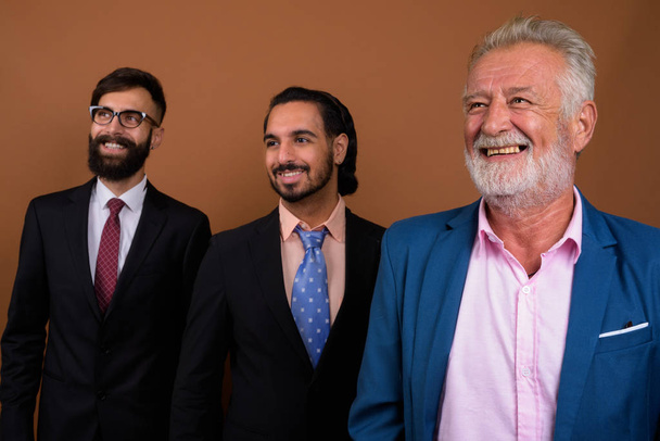 Tres hombres de negocios barbudos multi étnicos juntos contra el fondo marrón
 - Foto, Imagen