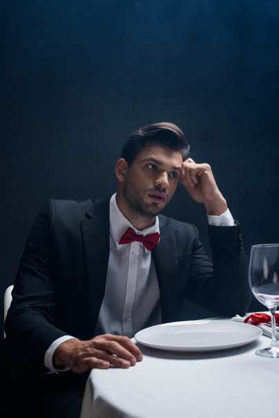 Handsome man in suit looking away at served table isolated on black - Фото, зображення
