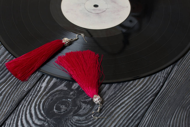 Homemade tassel earrings in red. Against the background of old vinyl records and brushed pine boards painted in black and white. - Foto, Imagem