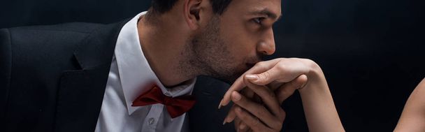 Panoramic shot of handsome man kissing hand of woman isolated on black - Photo, Image