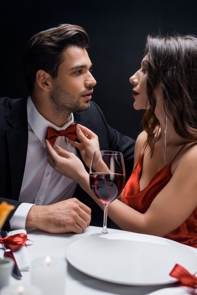 Mulher elegante ajustando laço gravata de homem bonito durante o jantar romântico isolado em preto
 - Foto, Imagem