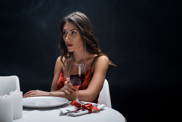 Piękna kobieta z kieliszkiem wina siedzi przy stole odizolowana na czarno - Zdjęcie, obraz