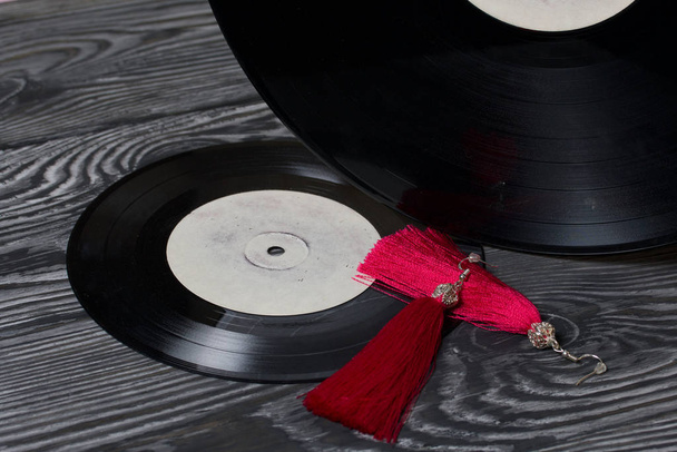 Homemade tassel earrings in red. Against the background of old vinyl records and brushed pine boards painted in black and white. - Photo, Image