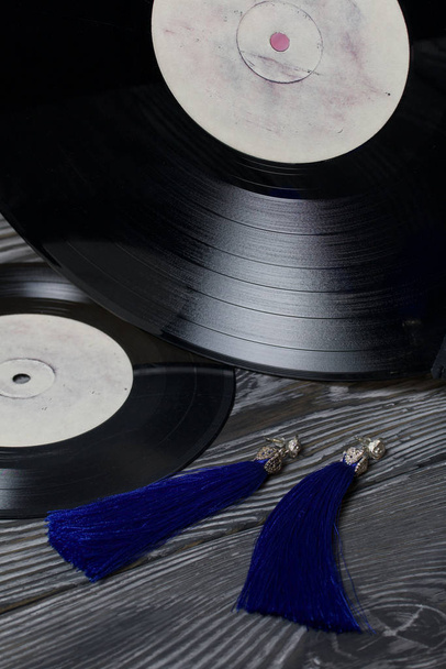 Homemade tassel earrings in blue. Against the background of old vinyl records and brushed pine boards painted in black and white. - Foto, Imagem