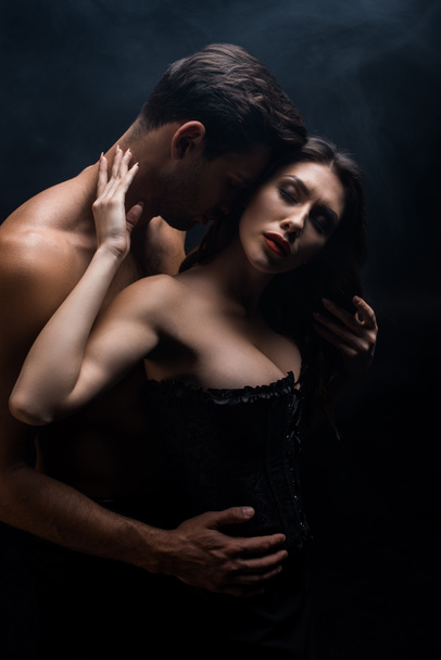 Muscular man touching sexy girlfriend in corset isolated on black - Fotografie, Obrázek