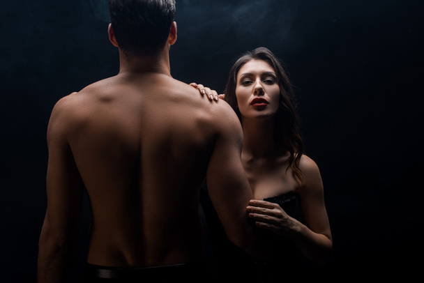 Сексуальная женщина, стоящая рядом с мускулистым парнем и смотрящая на камеру, изолированную на черном
 - Фото, изображение