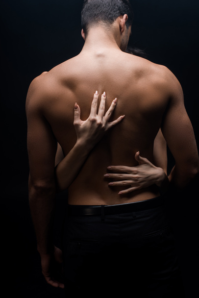 Woman hands touching muscular back of boyfriend isolated on black - Fotoğraf, Görsel