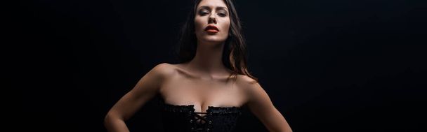 Panoramic shot of beautiful woman in corset looking at camera isolated on black - Foto, afbeelding