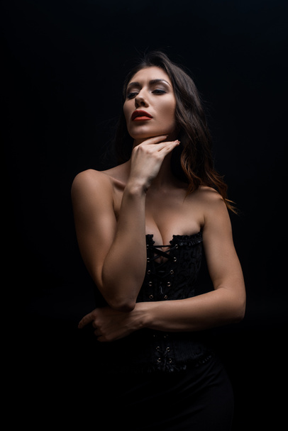 Sensual woman with hand by chin looking away isolated on black - Foto, Imagen