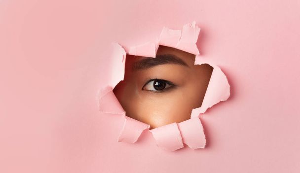 Asian female eye without mascara looking through torn paper - Foto, Imagem