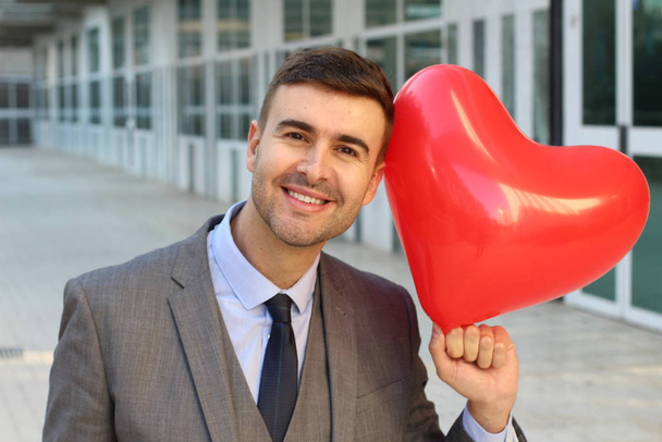 portrait de près d'un beau jeune homme d'affaires avec un ballon rouge en forme de cœur dans la rue - Photo, image