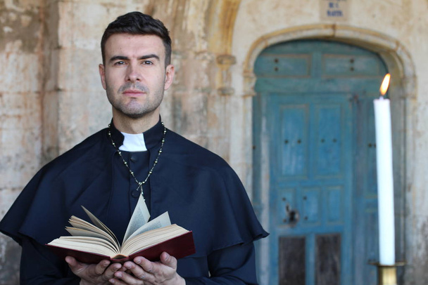 Σοβαρός ιερέας κρατώντας ανοιχτή τη Βίβλο στο φόντο της εκκλησίας - Φωτογραφία, εικόνα