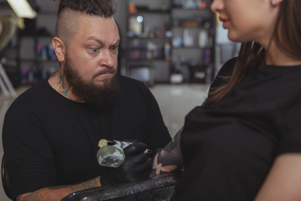 Молодая привлекательная женщина делает новую татуировку с помощью профессиональной татуировки
 - Фото, изображение