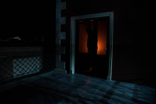 Η σιλουέτα ενός ανθρώπου μπροστά από ένα παράθυρο τη νύχτα. Τρομακτική σκηνή Απόκριες έννοια της θολή σιλουέτα του μανιακού. - Φωτογραφία, εικόνα