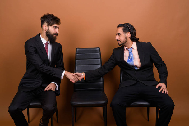 Dois empresários multi étnicos barbudos juntos contra fundo marrom
 - Foto, Imagem