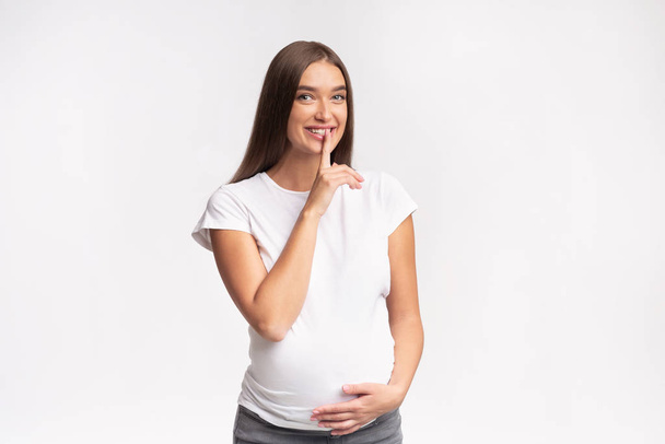 Gioioso incinta ragazza gesturing dito su labbra standing, studio girato
 - Foto, immagini