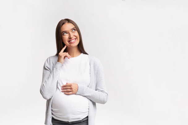 Vrolijke Moeder-To-be Dromen Staande Over Witte Achtergrond In Studio - Foto, afbeelding