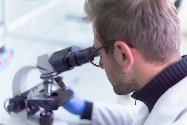 Fiatal férfi tudós, aki mikroszkóppal néz át egy laboroson. - Fotó, kép
