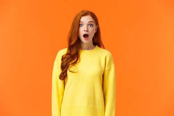 Shocked redhead cute girl drop jaw astounded and speechless, stare camera popped eyes, cant believe, standing impressed and fascinated, losing speech over orange background - Foto, Bild