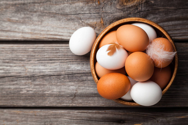 Fresh white and brown chicken eggs in a wooden bowl. Raw eggs on wooden background - Foto, Bild