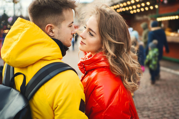Happy young couple looking at each other with smile, wearning in bright yellow and red down jackets. - Foto, afbeelding