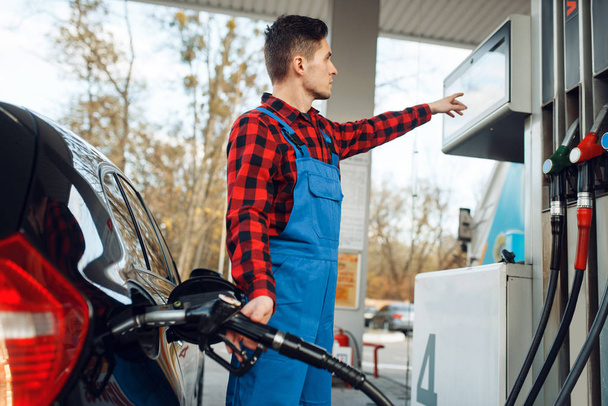 Mężczyzna w mundurze tankuje samochód na stacji benzynowej, tankuje paliwo. Usługi tankowania benzyny, benzyny lub oleju napędowego - Zdjęcie, obraz