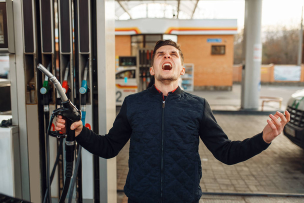 Depressiver Mann weint an Tankstelle, hoher Kraftstoffpreis. Benzinbetankung, Benzin- oder Dieselbetankung, Benzinbetankung - Foto, Bild