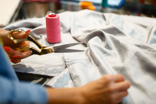 A varrónő ollóval vágja le a szövetet a textilboltban. Nő dolgozik ruhával varráshoz, női szabó műhelyben - Fotó, kép