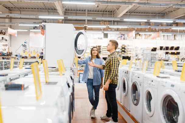 Family couple choosing washing machine in electronics store. Man and woman buying home electrical appliances in market - Foto, Bild