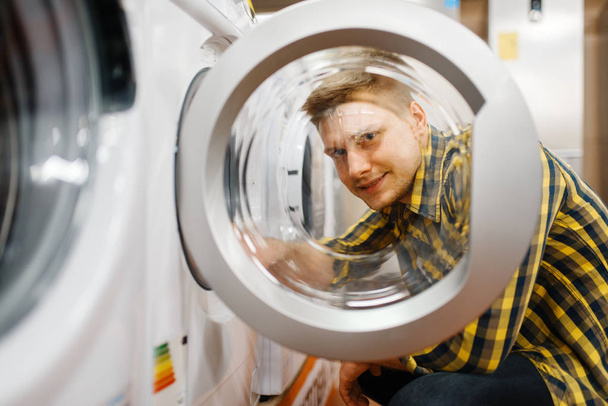 Man choosing washing machine in electronics store. Male person buying home electrical appliances in market - Fotó, kép