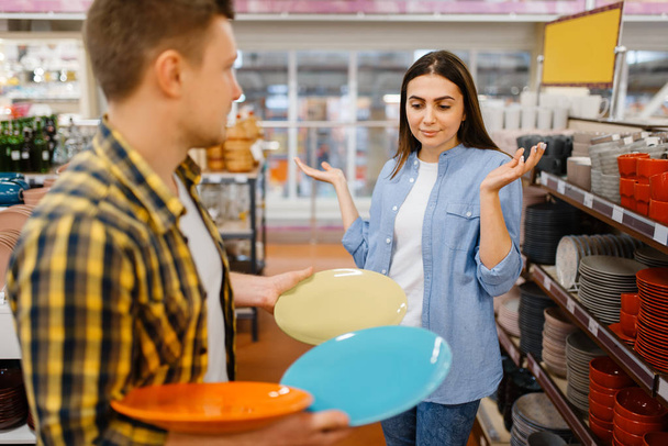 Mladý pár vybírá talíře v obchodě s nářadím. Muž a žena kupující domácí zboží na trhu, rodina v obchodě s nádobím - Fotografie, Obrázek