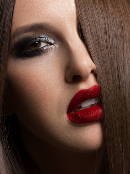 Close-up of the beauty of half a woman's face with fashion evening makeup. Black smoky eyes and long eyelashes, on puffy lips matte lipstick color wine. Clean skin after spa and long hair. Red lips - Fotografie, Obrázek