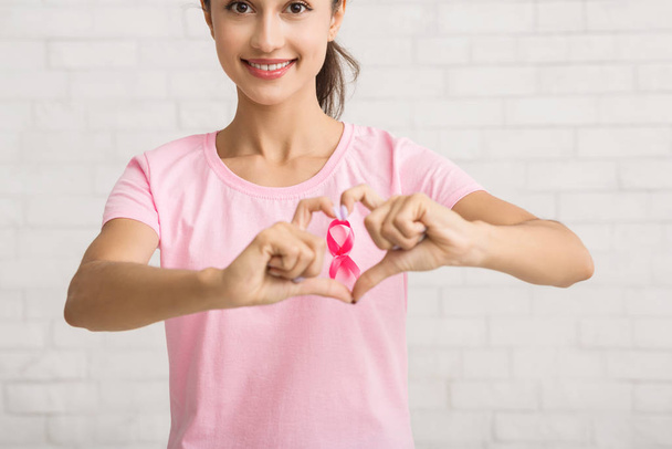Κορίτσι Gesturing σχήμα καρδιάς πλαισιώνει ροζ κορδέλα Σύμβολο Posing Εσωτερική - Φωτογραφία, εικόνα