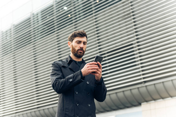 A young businessman walking and looking at his cell phone. - Foto, afbeelding