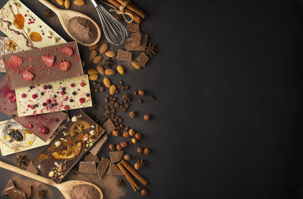 Handmade chocolate with berries, nuts, dried fruits on a dark background. Black and white chocolate. Chocolate bar. Chocolate background. Recipe. Copy space. - 写真・画像