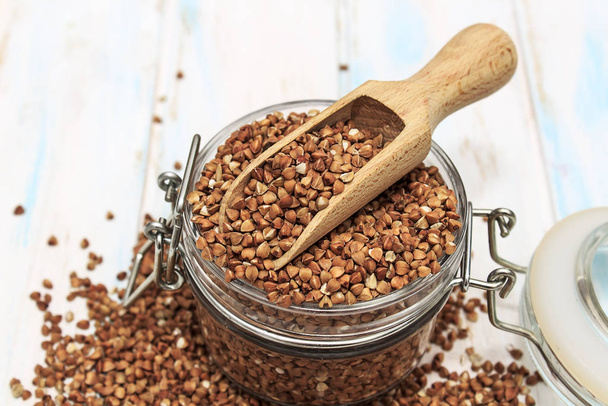 Buckwheat groats in a wooden spoon on a white wooden background. The concept of healthy nutrition and diet. Zero wast. Close-up. - Photo, Image