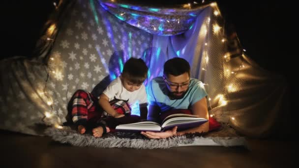 Отец и сын читают в палатке, установленной в помещении
 - Кадры, видео