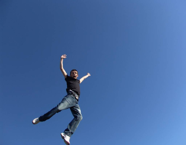 young man jumping against blue sky - Foto, afbeelding