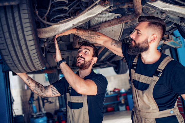 Два механика ремонтируют автомобиль в сервисном центре
 - Фото, изображение