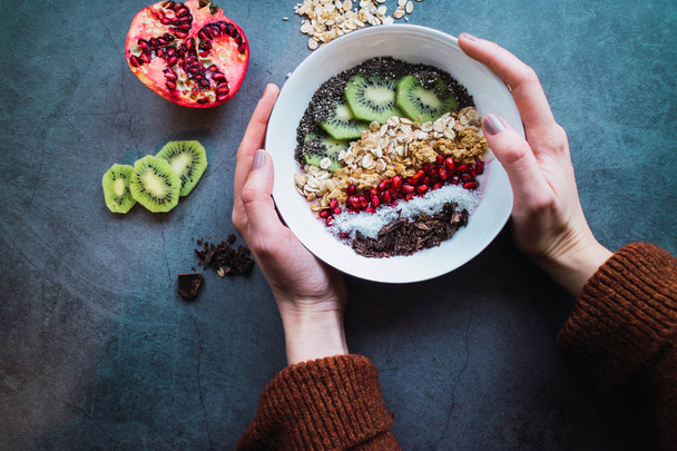 Healthy breakfast: Woman's hands holding a smoothie bowl with cereals and fruits. Flat lay. - Fotografie, Obrázek