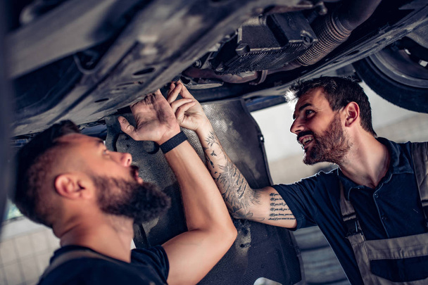 Dwóch mechaników naprawiających samochód w centrum serwisowym - Zdjęcie, obraz