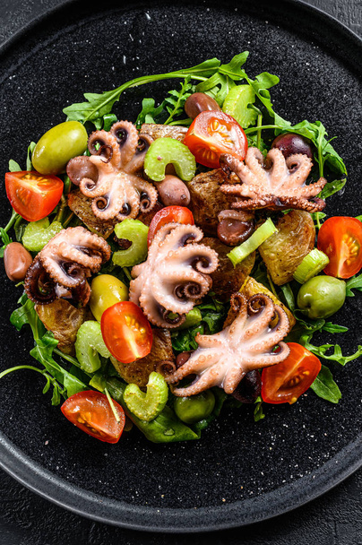 Salad with grilled octopus, potatoes, arugula, tomatoes and olives. Black background. Top view - Valokuva, kuva