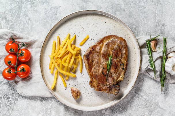 Grilled pork steak on bone with French fries. Gray background. Top view - Photo, Image