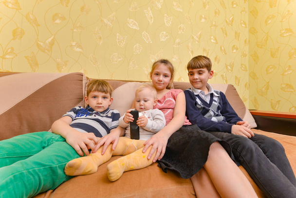 Vrolijke en vrolijke kinderen zitten op de bank in de woonkamer - Foto, afbeelding