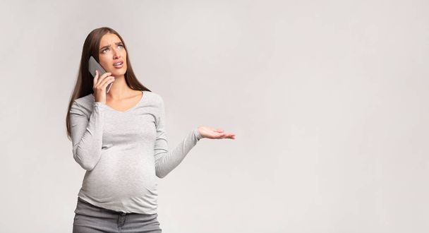 Mujer embarazada descontenta hablando por teléfono celular quejándose, fondo gris, Panorama
 - Foto, Imagen