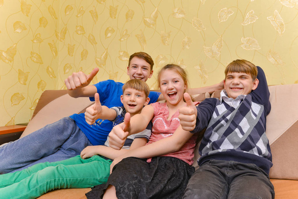 Szczęśliwe i radosne dzieci siedzą na kanapie i pokazują kciuk w górę - Zdjęcie, obraz