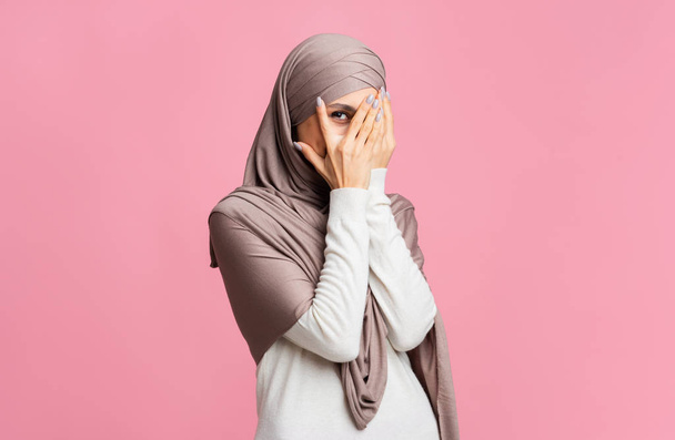 Shy arabic woman in hijab peeking through fingers with interest - 写真・画像