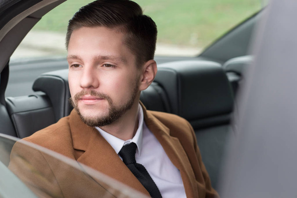 Sakallı bir gencin portresi. Yolcu koltuğundaki bir arabada iş adamı işe gitmek için ofise gidiyor. - Fotoğraf, Görsel