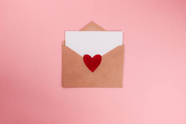 Love letter with white paper sheet in craft paper envelope with red heart flat lay on colorful pink background. 8 march, Mother's day, Valentine's Day template. Top view with copy space. Stock photo - Fotó, kép